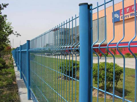 Blue curvy fence panels and peach posts are used beside the grassland.