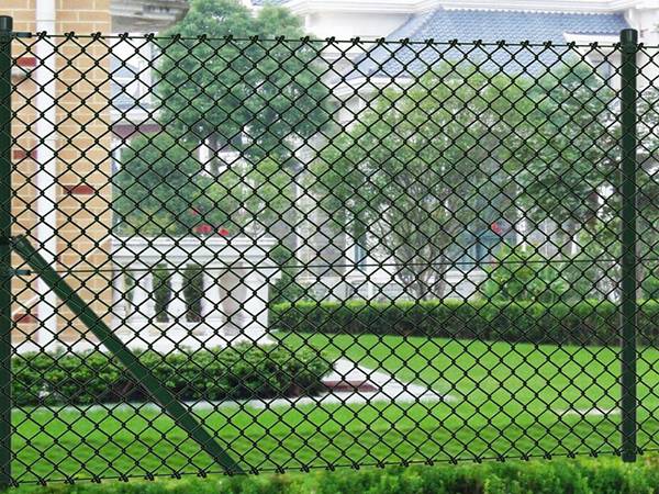 Black coated chain link fence with tension wire at the bottom in garden