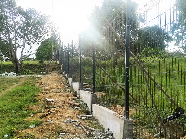 Wire mesh fence with posts installed on a concrete base along a slope.