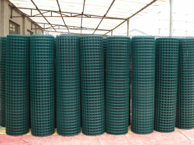 Many big rolls of PVC coated welded wire mesh in dark green are placed in workshop.