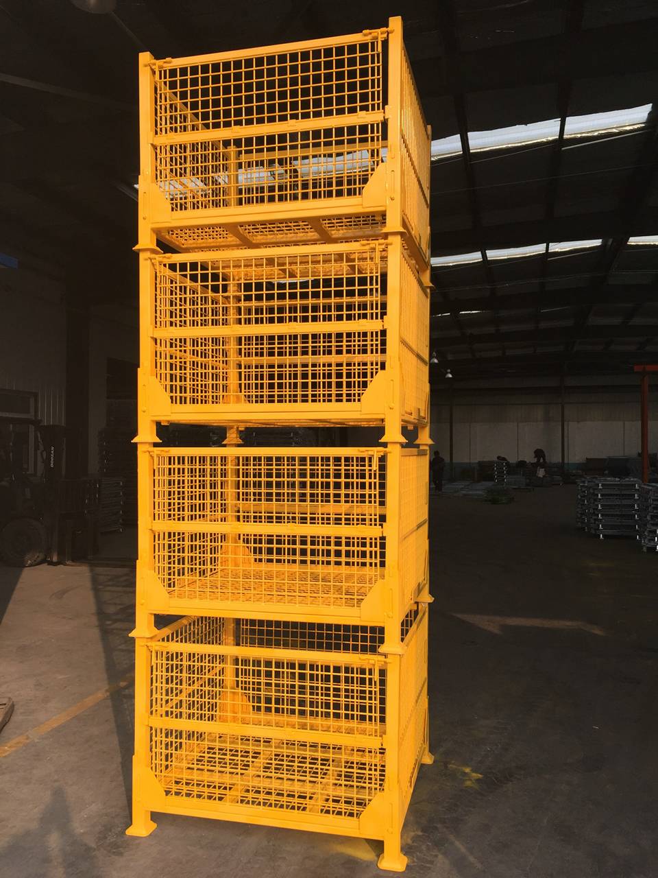 Four yellow welded wire container are stacked together in workshop.