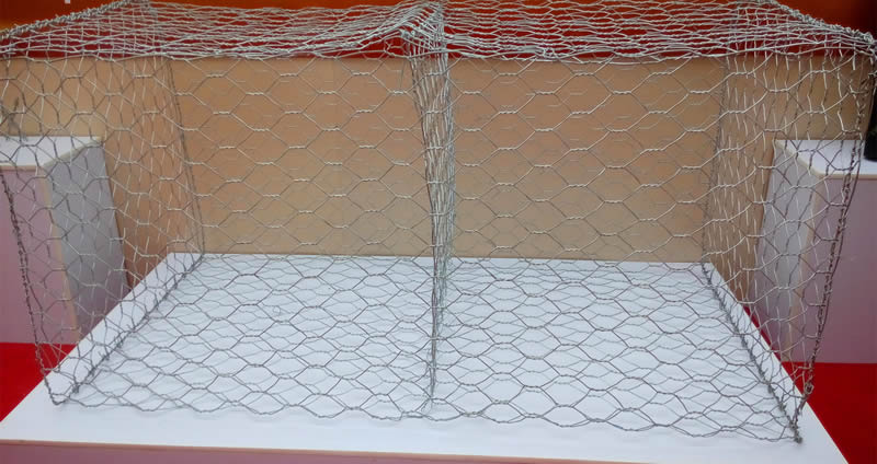 A galvanized gabion box with interlayer in the middle on a white stand.