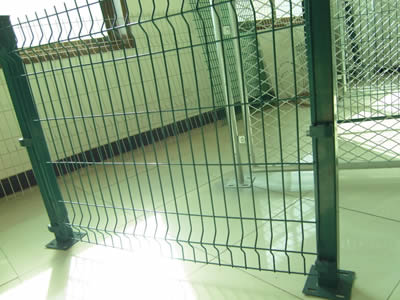 Green welded wire mesh fence with two post is placed on the floor.