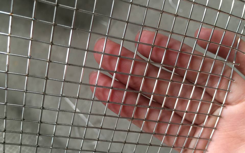 A hand is touching a piece of square hole stainless steel welded wire mesh.