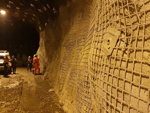Several workers are surveying in the tunnel and the tunnel walls are covered with welded coal mine support reinforcing mesh.